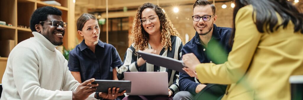 A diverse group of men and women with a positive mindset and smiles looking at digital devices.