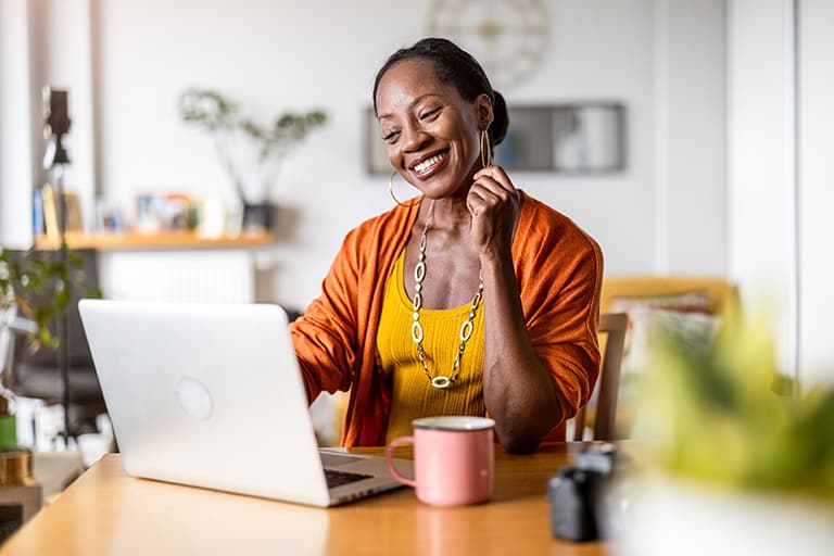 African American woman sitting at her kitchen table while using her laptop for a seamless, connected digital government experience.