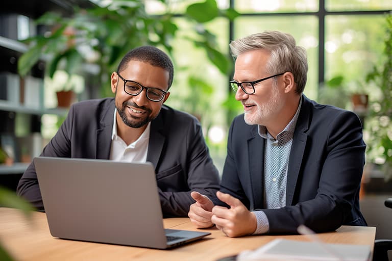 Two inspired male colleagues in casual suits working on a laptop in a bright room