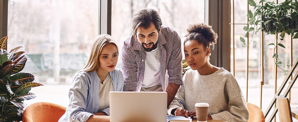 Three workers at table looking at laptop during a collaborative session