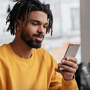 Young man wearing a yellow sweatshirt having a positive government experience on his mobile phone.