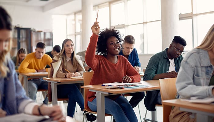 Feliz estudiante afroamericano levantando la mano para hacer una pregunta durante una conferencia en el aula.